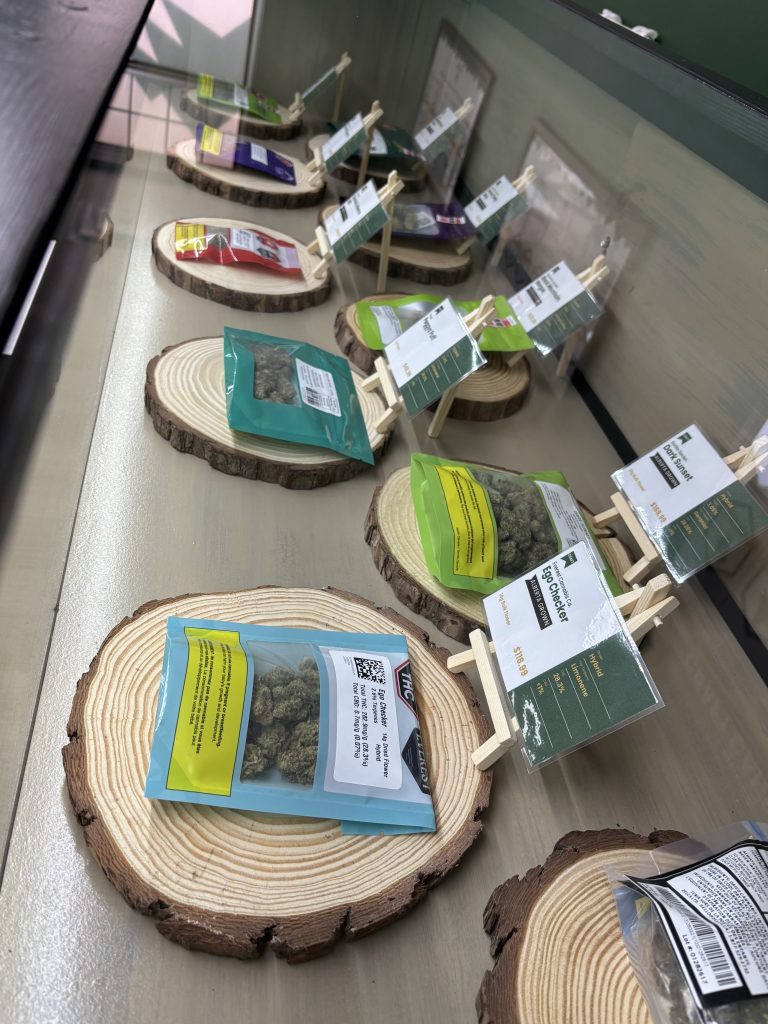 Cannabis products displayed in a glass case on wood-slice stands with price tags.